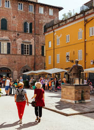 Two tourists walking over a town square in Tuscany