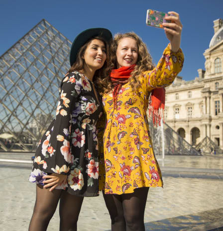 Two tourists taking a selfie in front of the Louvre