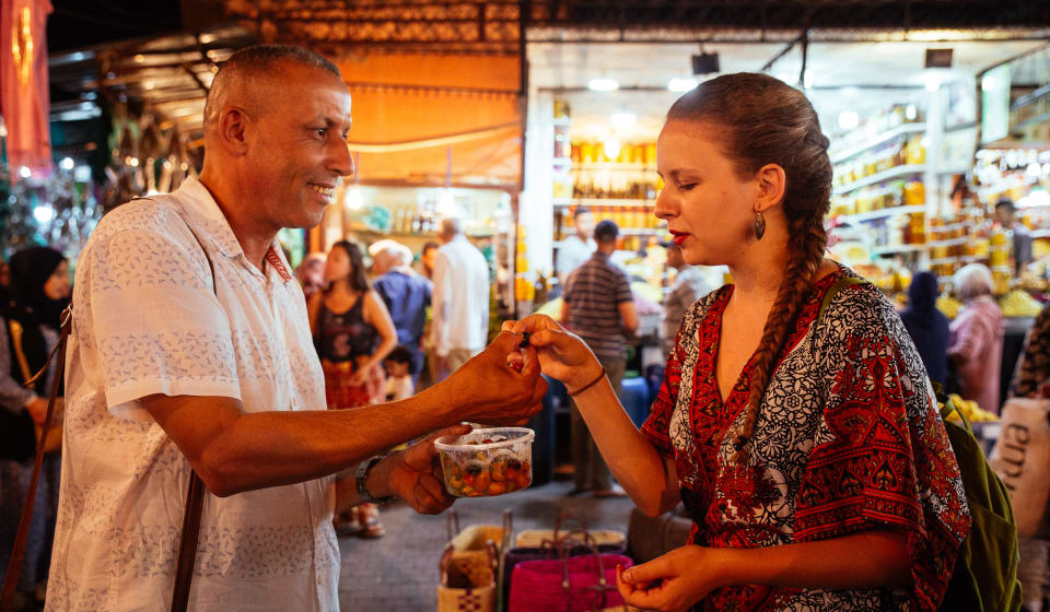 A street vendor offering dates to a lady on the busy streets of Marrakech in the evening