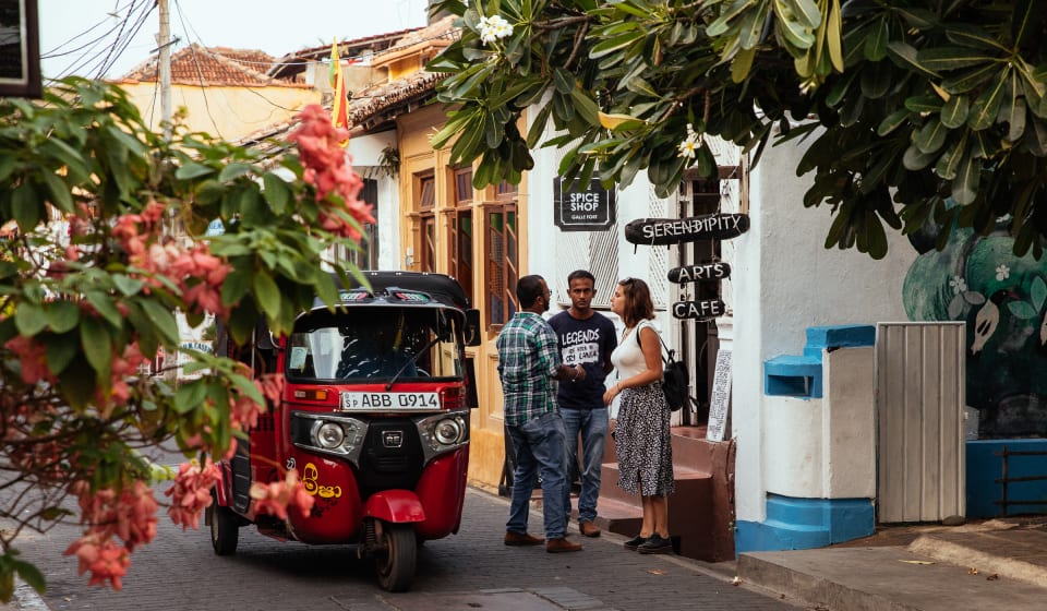 A tuk-tuk passing a local guide with two tourists on the streets of Colombo