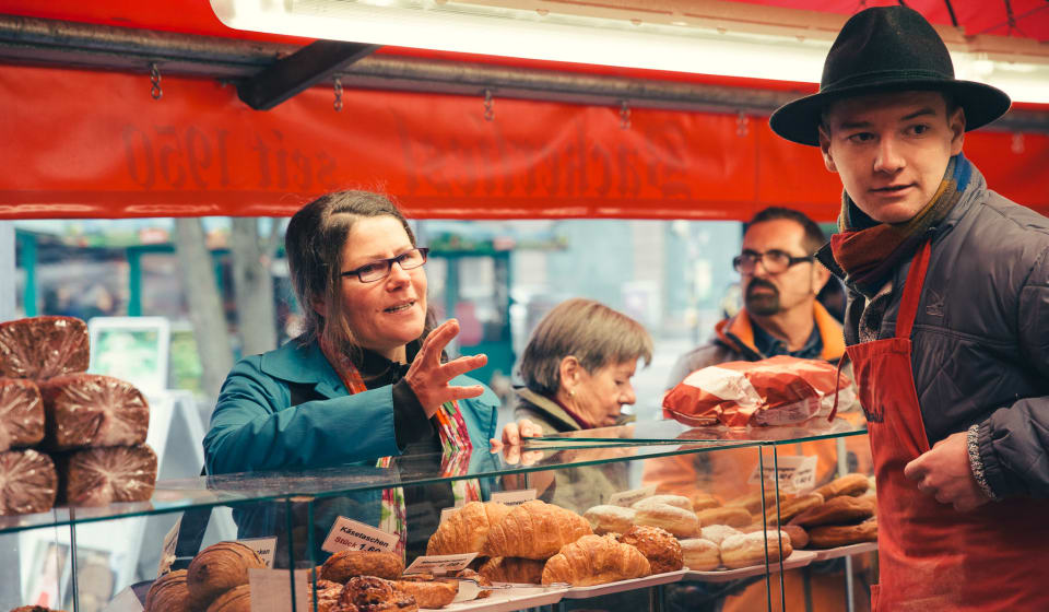 A woman ordering some bread at a market stall with a vendor