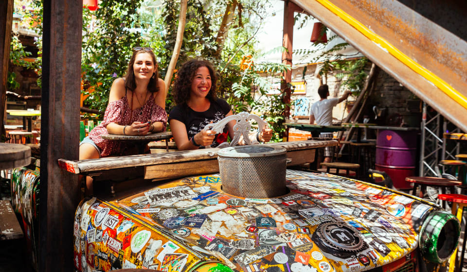 Two women sitting an old car frame full with stickers in Szimpla Kert