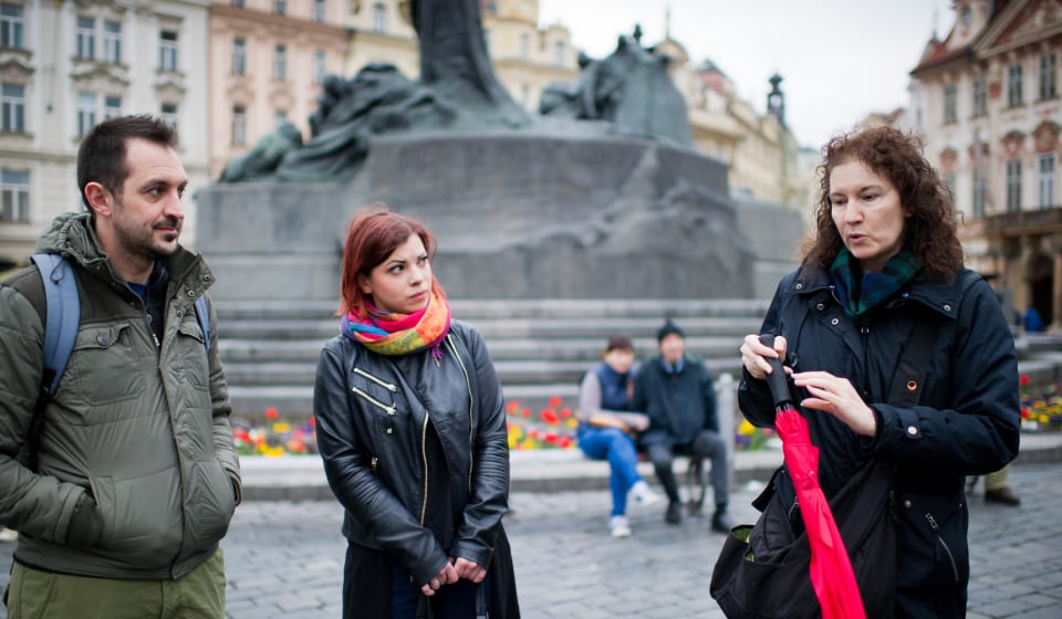 A local guide with a red umbrella telling a story to two tourists