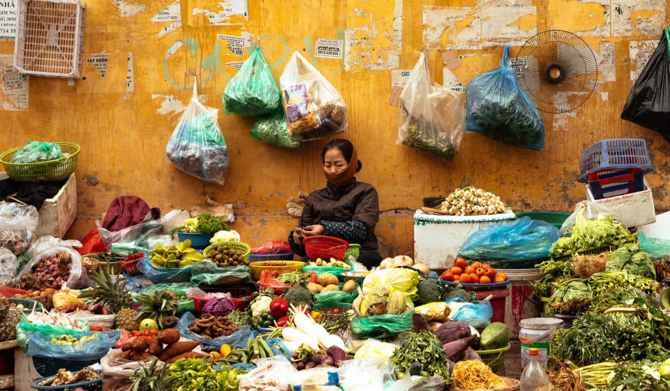 A vendor at a market stall with fresh produce at the Long Bien Market in Hanoi