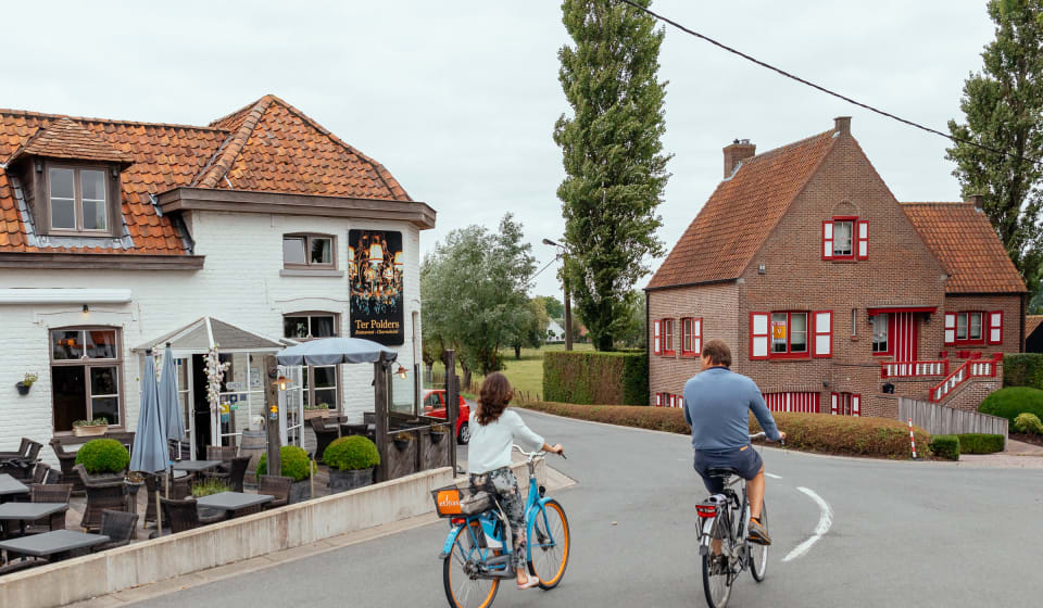 Two people cycling next to a pub near Bruges