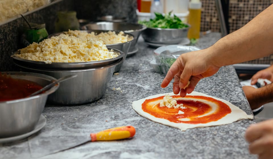A pizza is being prepared in a kitchen
