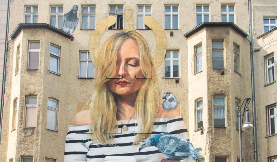 Murial on a building in Berlin of a woman with a smartphone in her hands and 2 pigeons and a sparrow looking at the phone