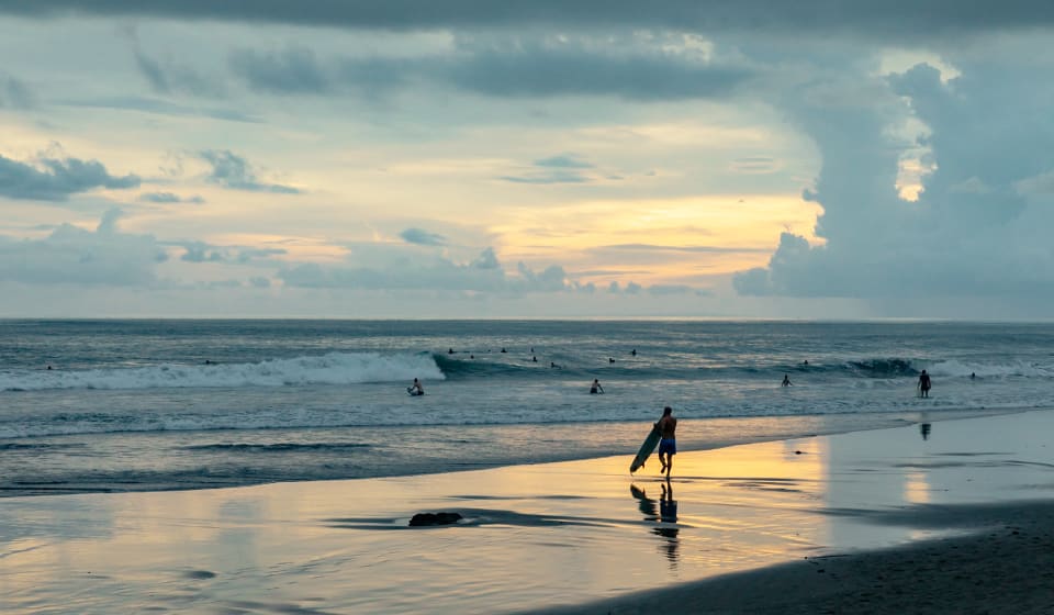 A view on the beach at Bali with people swimming and surfing
