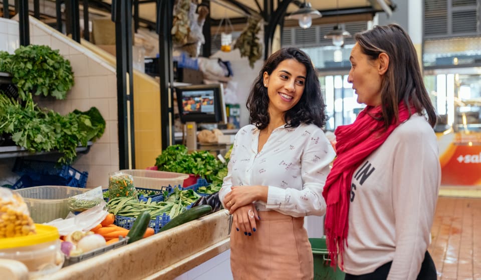 A local with a tourist at the Bolhão Market with a stall of local produce from Porto