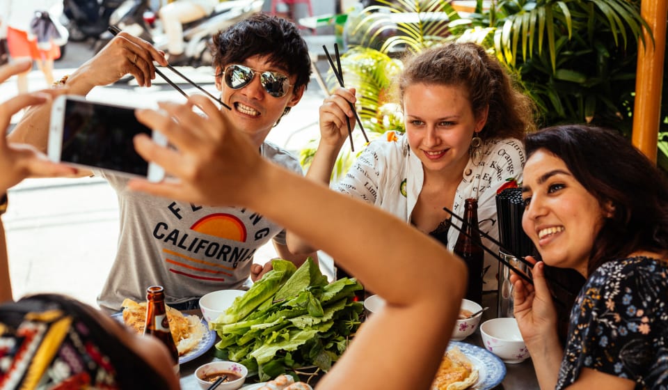 A group of tourists posing for a picture with food made in a cooking class at a home dinner in Ho Chi Minh City, Vietnam