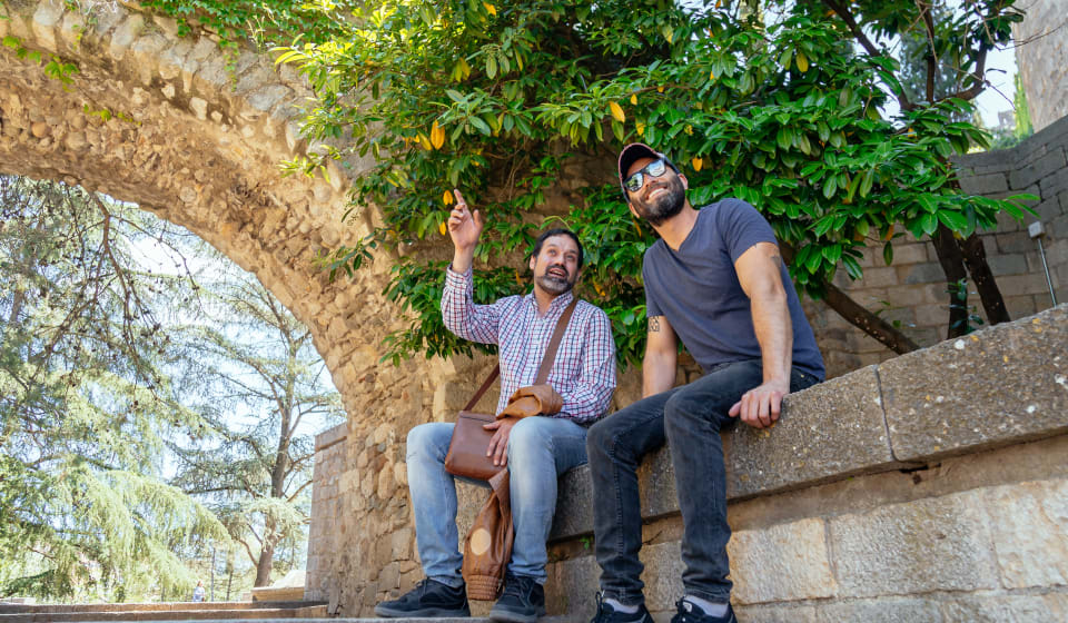 A local guide and a tourist sitting on an old wall near an old gate
