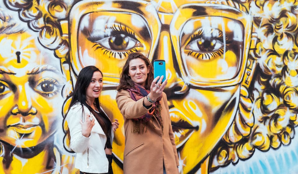 Two tourists taking a selfie at a graffiti murial in London