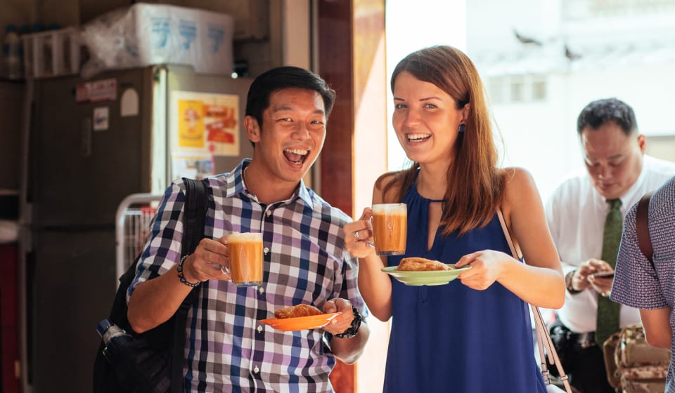 Two people with a drink and a plate of food smiling at the camera