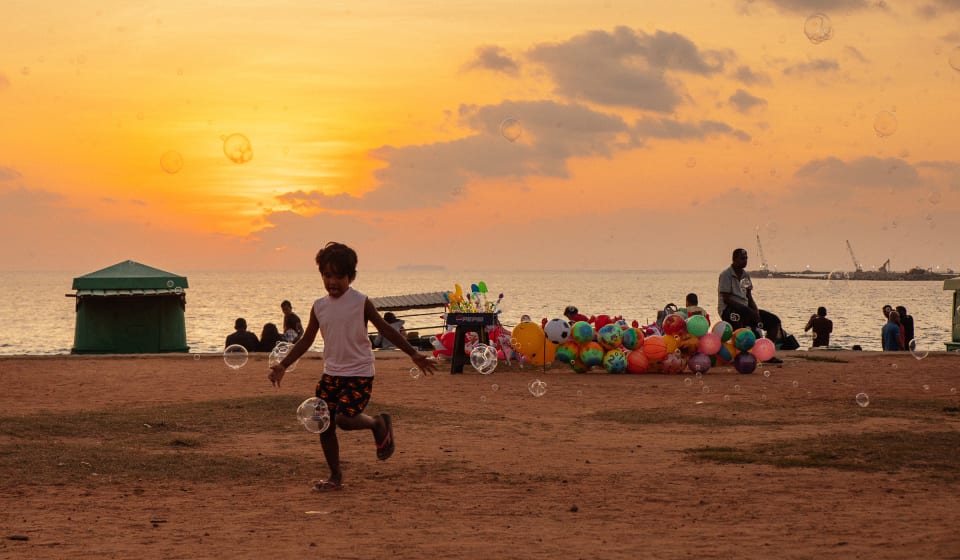 A child chasing bubbles at an ocean view park on Sri Lanka