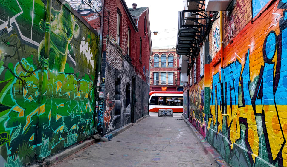 An alley in toronto with graffiti, at the end of the alley you are seeing a tram passing by
