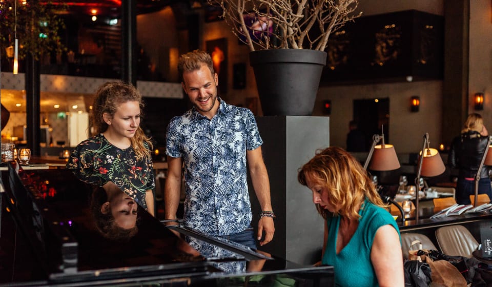 Two people watching someone playing a piano in a bar