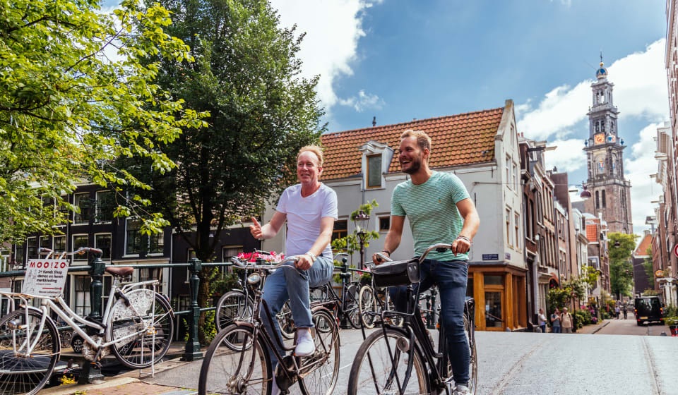 A local guide and a tourist on a bike crossing a bridge in Amsterdam