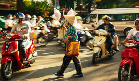 A local crossing the road between scooters and motorbikes in Ho Chi Minh city