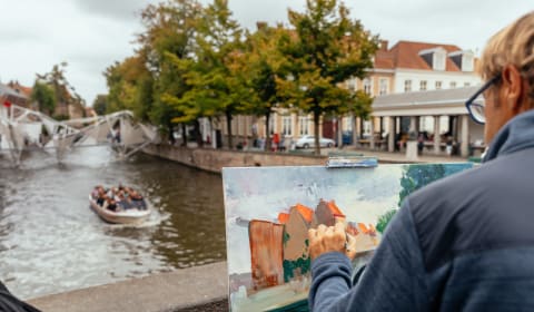 A man painting a bridge in Bruges with a view on the water with a boat