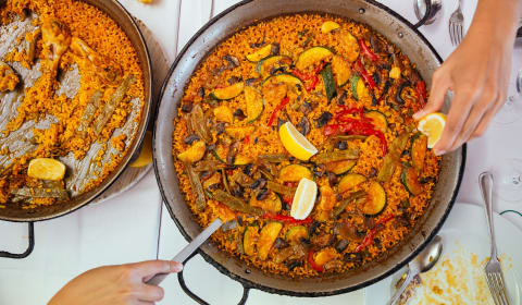 A top down view of a pan of paella with someone stirring the pan and squeezing a lemon above the pan