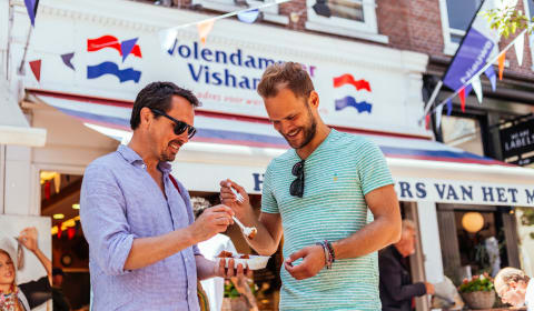 A local guide and a tourist tasting Kibbeling on a local food tour in Amsterdam on the Albert Cuyp Markt