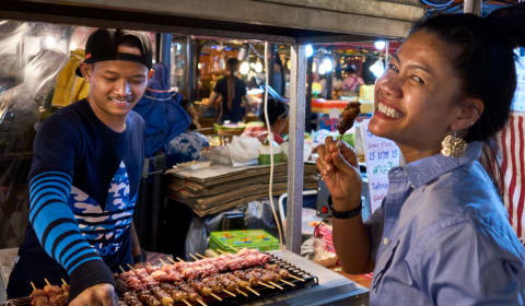 A local tasting saté a the Bangkok market a street food stall with a vendor