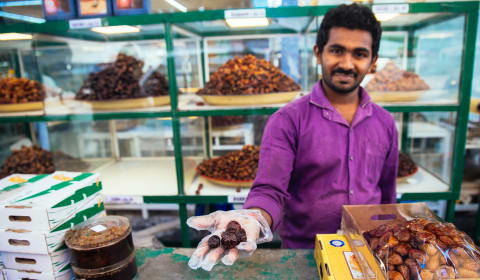 A vendor at a market stall showing dates in his hands