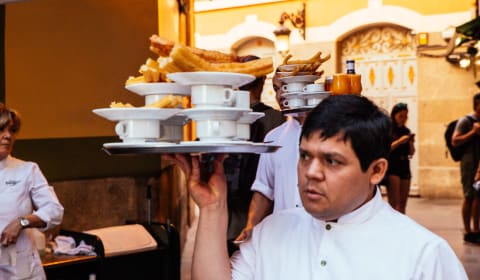 A waiter at Plaza Mayor with a tray full of churros and chocolate filled cups in Madrid