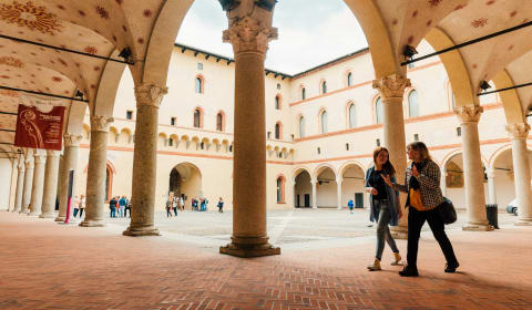 A local guide and a tourist walking through the courtyard of Castello Sforzesco in Milan