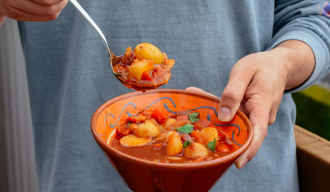 Someone holding a bowl of Gulash with a full spoon on top