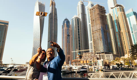 Local guide and a tourist making a selfie with a selfie-stick. The background is the skyline of Dubai