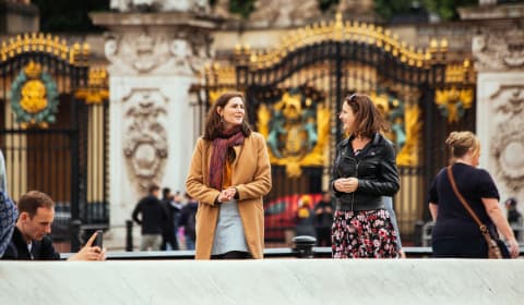 A local guide and a tourist walking near the gates of Buckingham Palace in London