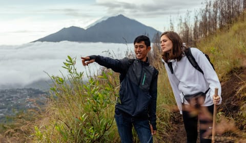 A local guide showing a tourist a beautiful viewpoint on Mount Batar, Bali, with a mountain in the back
