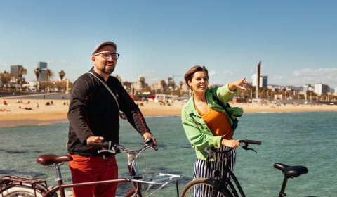 A local host and a tourist with bikes at the beach of Barcelona