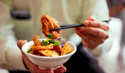 A bowl of Taiwanese food with some chicken in chop sticks above the bowl