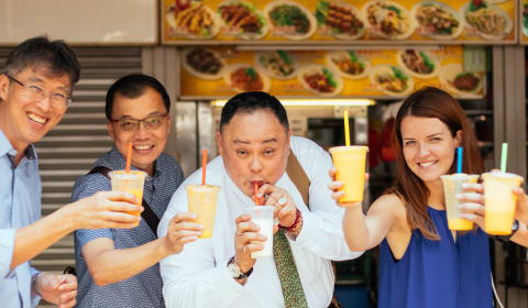 A group of people posing with a milkshake in front of a food stall in Singapore