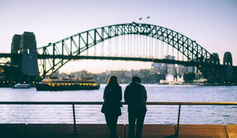 Two people looking at the Harbor Bridge in dusk