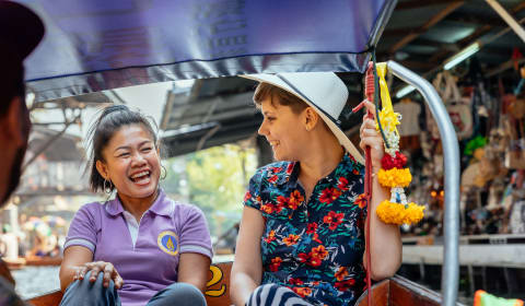 A tourist and a local laughing on a boat at a river in Bangkok