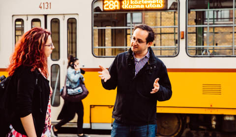 A local guide telling a story to a tourist with a tram on the background in Budapest